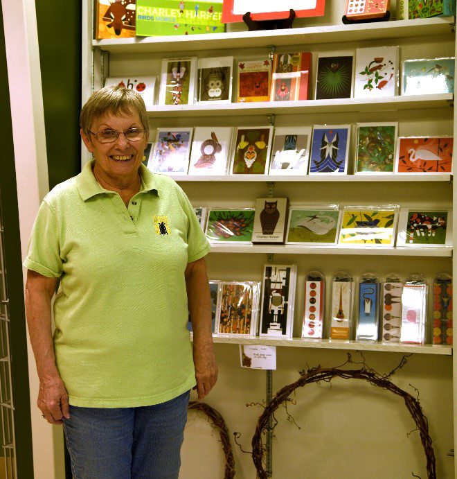 A woman standing in front of a wall containing postcards, cards, puzzles, and other Charlie Harper items.