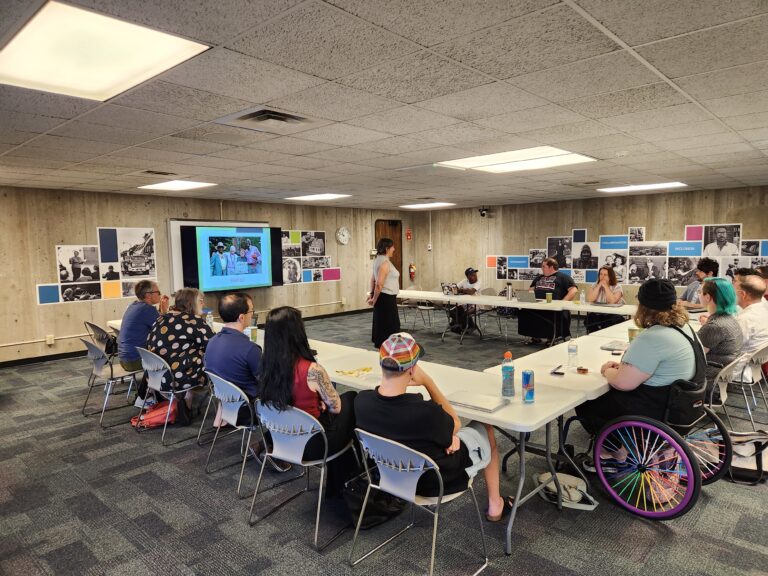 A photo of the GOHI Community of Practice sitting around a circle. In the center is Dr. Susan Ferentinos, who is presenting on best methods in LGBTQ+ research.