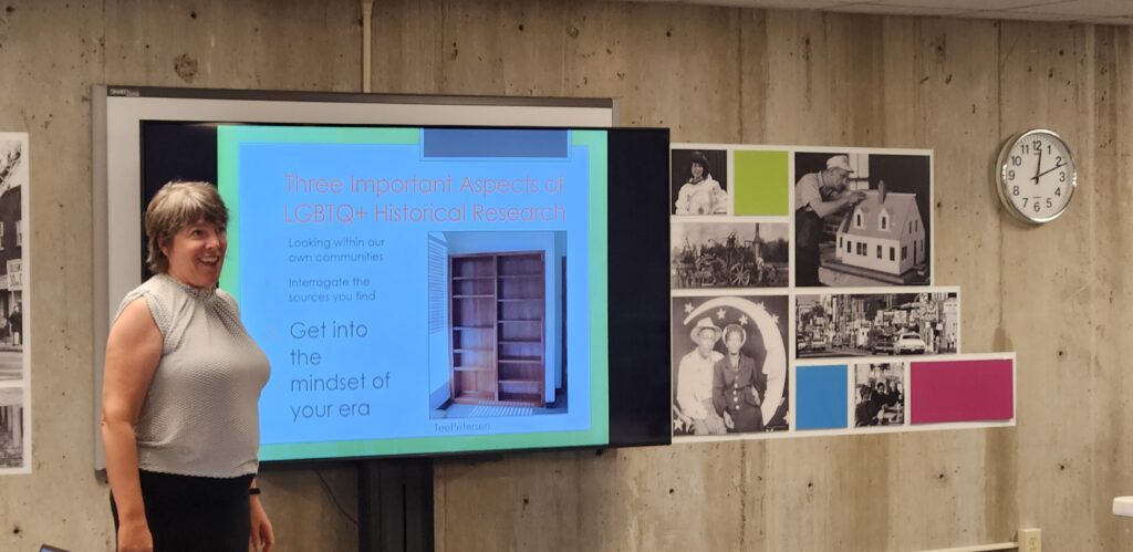 Photo of Dr. Susan Ferentinos in front of a screen that features her presentation on researching LGBTQ+ local history. Dr. Ferentinos is smiling. 