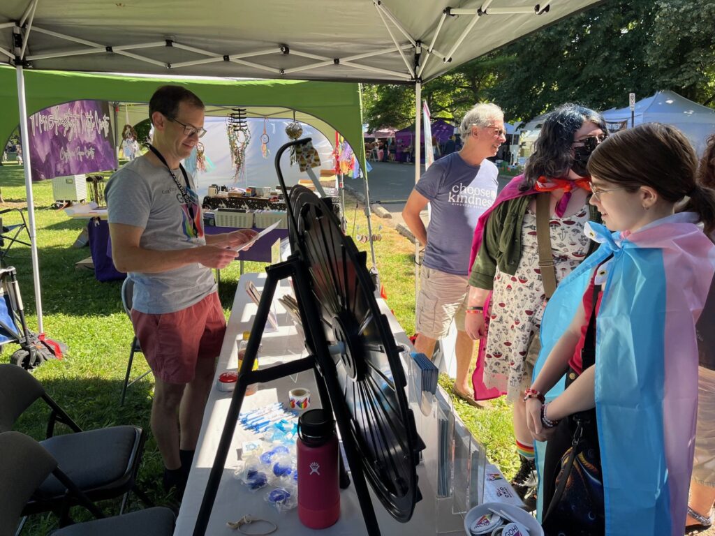 A photo of one of our GOHI Staff reading a history trivia question to visitors at our GOHI table at Columbus Pride, 2024.