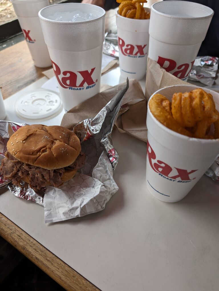 Image of a meal from Rax including a roast beef sandwich, curly fires, and a cup of ice water.