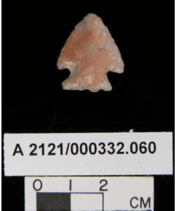 This is a projectile point approximately two centimeters long. It is made of a slightly glassy type of rock and has mottled pink and grey coloring. 