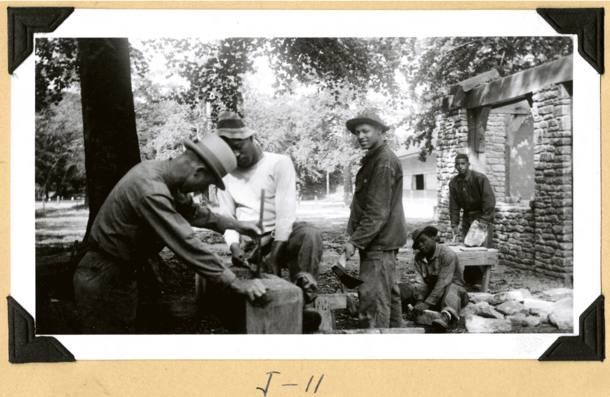 Group of men in 1930s clothing using tools to shape wooden beams