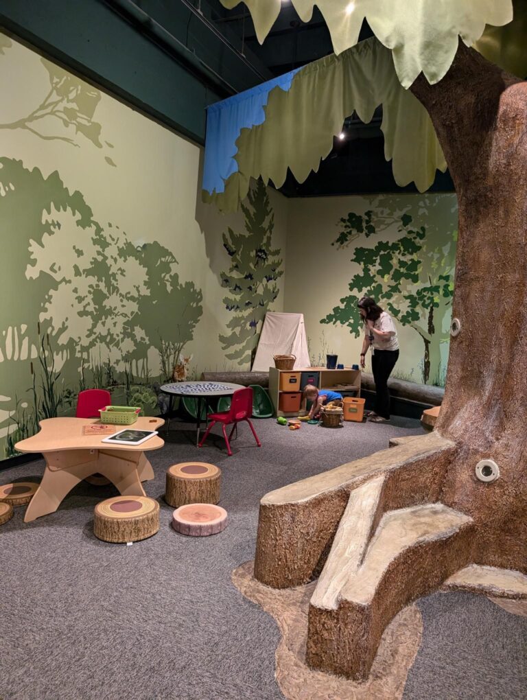 Children's play area with two tables on the left side and a fake tree on the right.