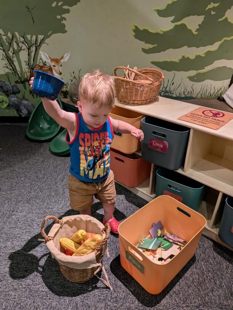 Child holding a pot standing behind two baskets of toys.