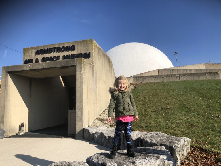 A small child standing in front of the entrance to the Armstrong Air and Space Museum