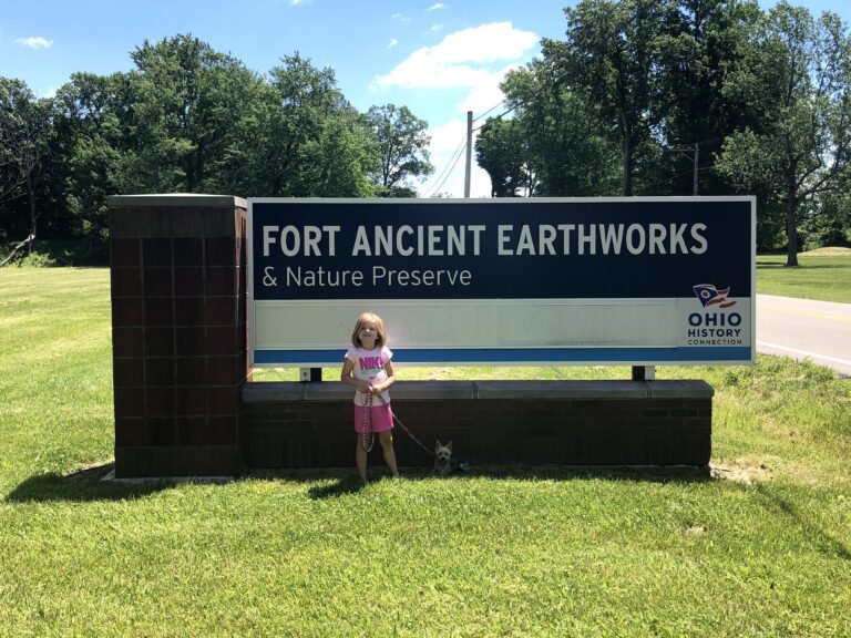 A small child standing in front of the welcome sign at Fort Ancient Earthworks & Nature Preserve