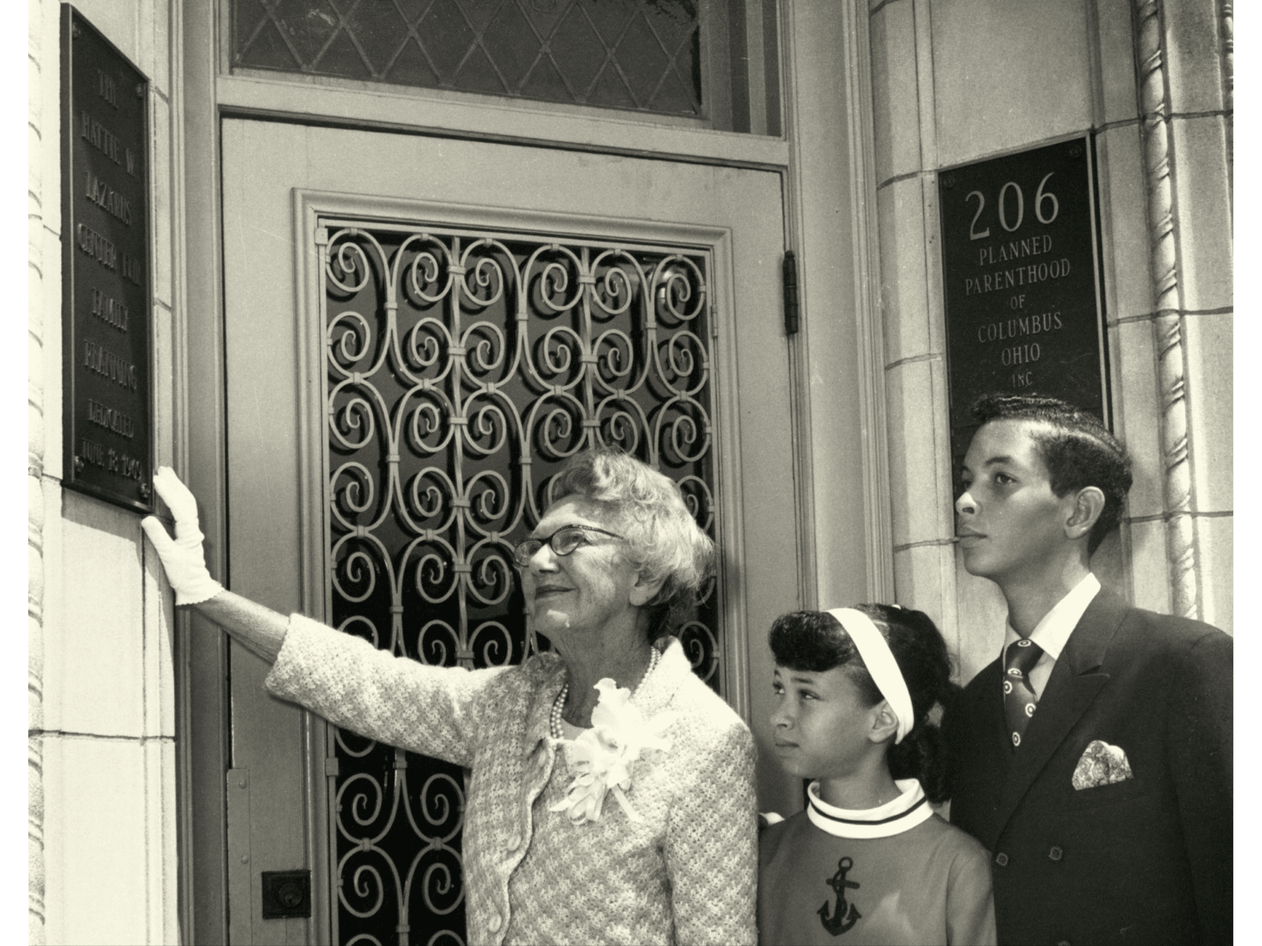 Black and white photograph of Hattie Lazarus and two young people standing in front of the Hattie Lazarus Center for Planned Parenthood of Central Ohio.