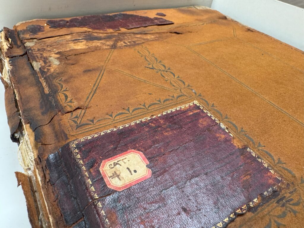 Faded and worn brown cover of a ledger book with "cat. 1" written on a small cream and red label